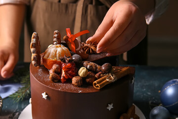 Woman decorating tasty Christmas chocolate cake at table, closeup