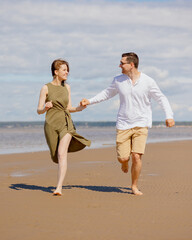 a couple of a man and a woman are walking on the beach or running along the sand along the seashore. beautiful and young European man and woman on a romantic walk in nature, a couple in love, a happy