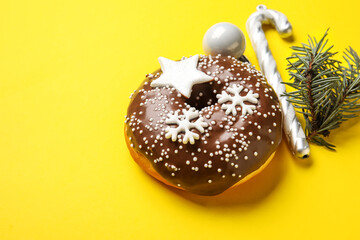 Tasty Christmas donut with fir tree branch, ball and candy cane on yellow background, closeup