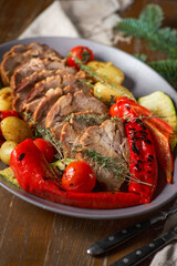 Sliced cooked pork neck on a plate with baked vegetables and potatoes on a wooden rustic table