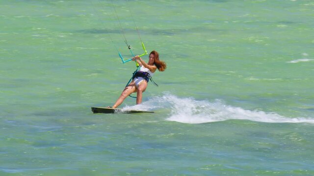 A beautiful young girl in a white swimsuit rides the waves on a kite on a clean and transparent ocean