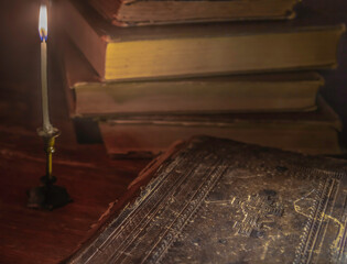 Candle light illuminates the books with the bible in the foreground