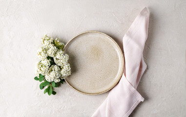 Ceramic plate and pink napkin, flower on a beige stone table. Top view, copy space. Table setting, menu background, mockup, recipe background, flat food mockup
