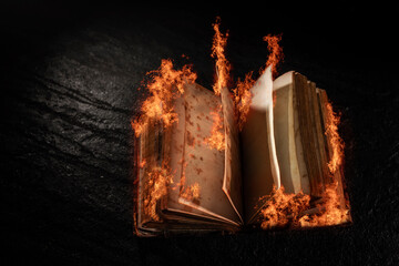 Open old book with burning pages on dark background