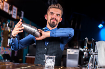 Young barman mixes a cocktail on the bar