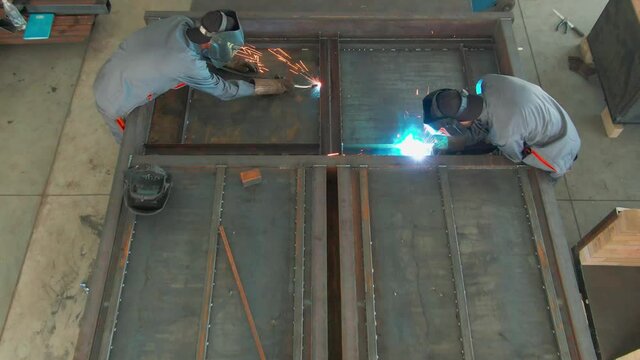 Two welders in protective masks works with metal steel and iron using a welding machine, bright sparks and flashes. Work in the shop. Video from above. 4k