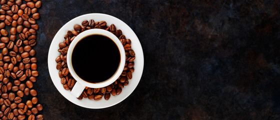 Cup of black coffee on a white saucer and coffee beans. Coffee and roasted coffee beans on a dark background. Coffee background. Panoramic shot