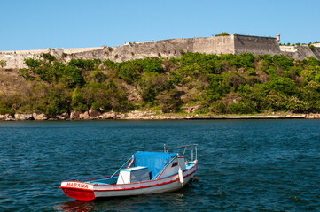 Fototapeta na wymiar Fishing boat anchoring at the entrance to the port of Havana with the wall of a fort from the Spanish colonial era in the background. Cuba.