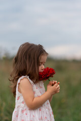 Beautiful cute girl wearing dress smelling big red flower. 