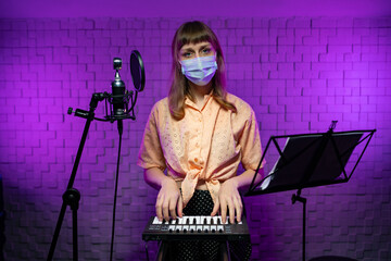 A female DJ stands on stage behind a keyboard, a music stand and a microphom in a protective mask. Party during the pandemic