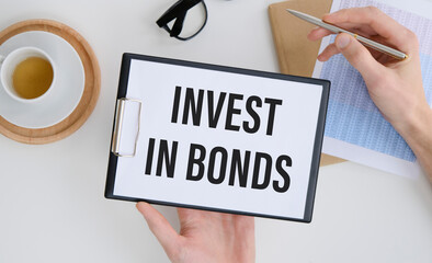 Closeup on businessman holding a card with INVEST IN BONDS message, business concept image with soft focus background