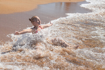 A little girl bathes in sea water on a sandy shore. Summer vacation at the sea