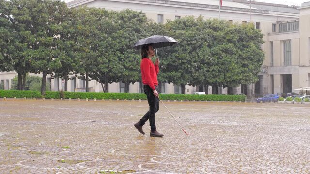 young man with a disabiity walks alone in the rain with cane and umbrella