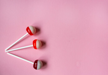 Set of three pink, red and white sweet delicious lollipops on white plastic sticks on pink pastel background.