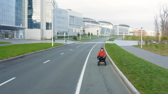 VLADIVOSTOK, RUSSIA - NOVEMBER 5, 2021: Aerial view of a man with amputated legs and arms driving on electric wheelchair along the empty street in Far Eastern Federal University campus area