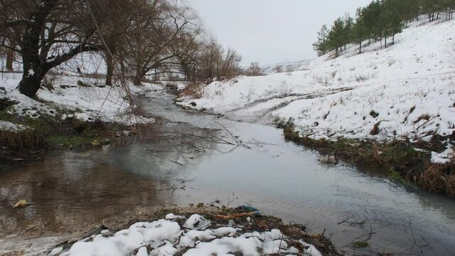 Winter river. Dirty water enters the river channel through a pipe. Sandy bottom.