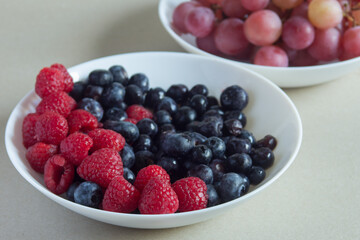 A close-up of a few raspberries in several plates with fruits of the forest on a textured surface. Natural ingredients and healthy food.