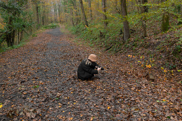 A photographer girl taking nature in autumn. She has brown hat. Leaves on ground. Hobby concept. Unrecognizable person.