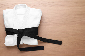 Martial arts uniform with black belt on white wooden background, top view. Space for text