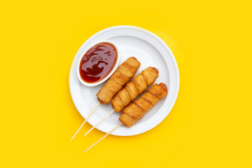 Fried dough snacks wrapped sausage in white plate on yellow background.
