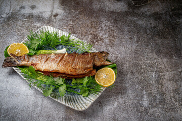 Roasted Whole Trout with lemon, lettuce and dill and parsley greens on a plate against a gray stone table