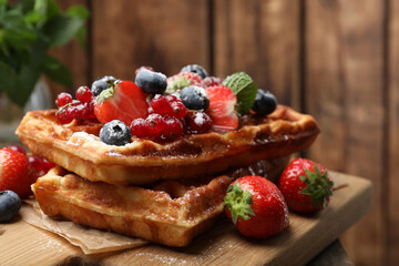 Delicious Belgian waffles, berries and powdered sugar on wooden board, closeup