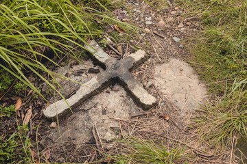 A old concrete cross in the ground marks an unmarked grave or burial site under the ground. At a public cemetery at the Philippines. - obrazy, fototapety, plakaty
