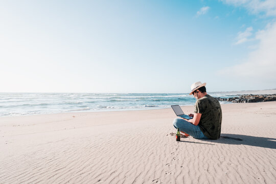 Man Sitting On The Beach Drinking Beer With Laptop Alone Doing Telecommuting