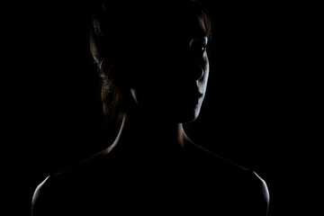 silhouette contour of a beautiful brunette girl. Side lit studio portrait on dark background.