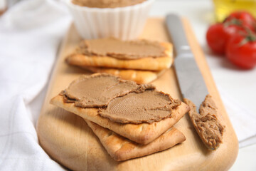 Crispy crackers with delicious meat pate and knife on wooden board, closeup