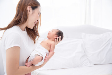 Asian loving mom carying of her newborn baby at home. Happy mum holding sleeping infant child on hands. Mother hugging her little one months old son.