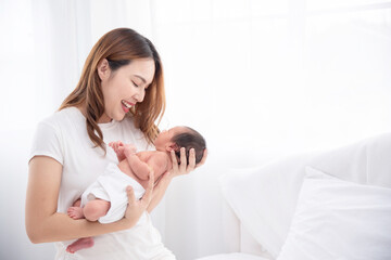 Asian loving mom carying of her newborn baby at home. Happy mum holding sleeping infant child on hands. Mother hugging her little one months old son.