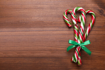 Bunch of sweet Christmas candy canes with bow on wooden table, top view. Space for text