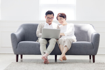 Middle-aged couple sitting on a sofa in the living room at home and working on a laptop