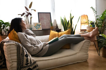 Caucasian woman lying on the couch relaxing reading a book at home. Copy space.