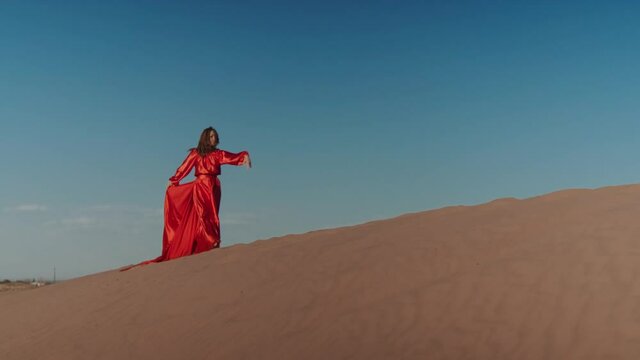 An Asian woman in a red dress dancing on sand dunes