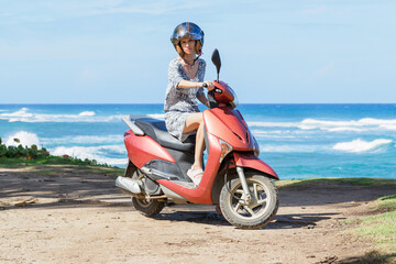 Fototapeta na wymiar Woman wearing helmet riding a scooter on a tropical island next to ocean.