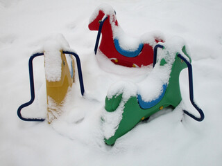 A bright snow-covered carousel for the youngest children, consisting of three funny plastic horses,...