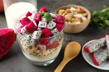 Glass of granola with different pitahayas, yogurt and other fruits on grey table, space for text