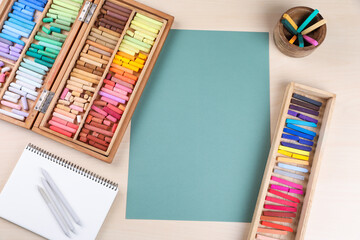 Layout with blank paper, soft pastels and other drawing supplies on wooden table at artist's workplace, top view. Space for design