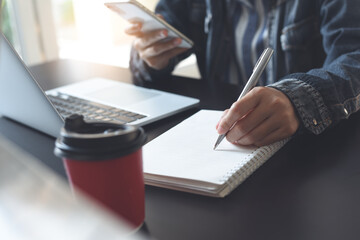 Woman working on laptop computer and mobile phone, writing on notebook in coffee shop, Student learning online class