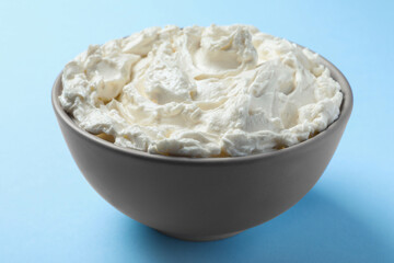 Bowl of tasty cream cheese on light blue background, closeup