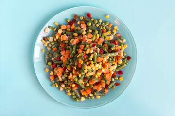 The concept of using quick-frozen products. Frozen vegetables in a light plate on a bright blue background top view.