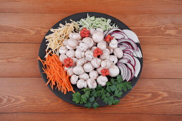 Obraz na płótnie Canvas Fresh mushrooms and champignons. Laid out on a round black plate. Onion, Carrot, Cucumber, Parsley, Cheese. For table setting. On a wooden background. Top view. Close-up. A sprig of greenery.