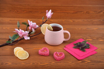 Pink cup of tea with lemon for breakfast.on Valentine's Day. valentine's day.An orchid flower on a branch. Pink napkin. lime leaves. candles in the shape of a heart. Still-life. on a wooden background