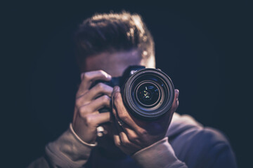 A man photographer with a camera takes a photo in the dark. - Powered by Adobe