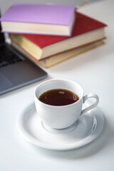 Obraz na płótnie Canvas Cup of tea with saucer on the table near books and laptop.