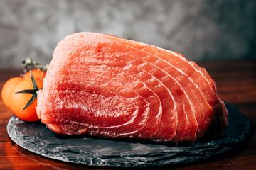 piece of tuna on slate plate with tomatoes on gray background. selective focus. copy space