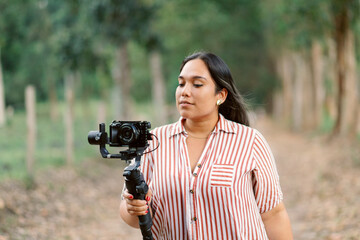 Hispanic woman holding a camera for a vlog against a blurred background