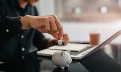 Business man holding coins putting in glass with using  laptop to calculate concept saving money for finance accounting.